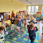 Dzieci tańczą z misiem na dywanie.