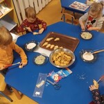 grupa dzieci siedząca przy stole_ dekorująca ciasteczka lukrem i posypką.