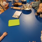 dzieci przy stolikach. Na stole produkty spożywcze i narzędzia kuchenne do przygotowania ciasteczek.