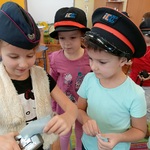 Troje dzieci w czapkach konduktorskich bawi się kasownikiem biletowym.