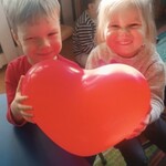uśmiechnięty chłopiec i dziewczynka trzymają czerwony balon w kształcie serca.