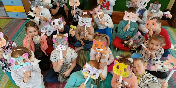 Przedszkolaki trzymają maski kotów i robią śmieszne miny.