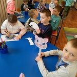 Przedszkolaki siedząc przy stolikach wykonują maski kotów.