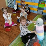 Kilkoro dzieci siedzi na podłodze z pluszowymi kotkami i talerzykami z chrupkami.