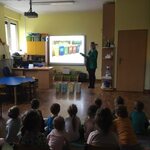 dzieci siedzą na dywanie na przeciwko ekranu ogladając prezentację.
