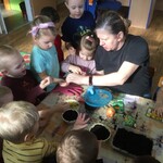 dzieci siedzą wokół stołu kobieta sypie im ziarenka na ręce.