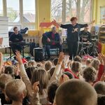 Przed dziećmi znajduje się grupa muzyków_ kobieta prowadząca oraz instrumentaliści 