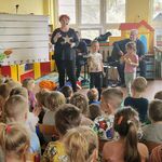 Obok muzyków stoi troje dzieci z instrumentami.