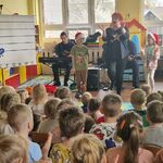 Po obu stronach kobiety prowadzącej stoją dzieci w czapkach Mikołaja.