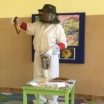 kobieta ubrana w strój pszczelarza pokazuje plaster miodu