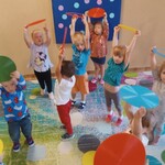 grupa dzieci trzymająca krążki nad głowami_ w tle tablica w kolorowe kółka