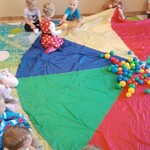Siedzące dzieci wokół chusty animacyjnej_ na środku chusty kolorowe piłeczki