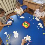 Dzieci siedzą przy stoliku i naklejają kolorowe kropki