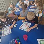 Dzieci siedzą przy stolikach i malują kropki