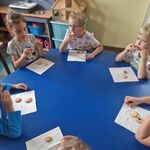 Dzieci siedzą przy stoliku i degustują upieczone okrągłe ciasteczka