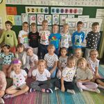 Grupa dzieci w kropkowych ubraniach prezentuje się na tle tablicy