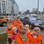 Dzieci ustawione parami stoją na chodniku między samochodami