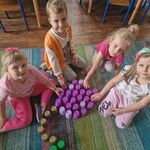 Czworo dzieci prezentuje śliwkę ułożoną na dywanie z kolorowych kubeczków