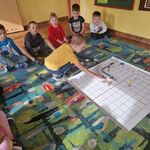 Dzieci siedzą na dywanie_ a chłopiec układa na macie drogę wg kodu
