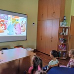 Dzieci siedzą na krzesełkach i oglądają film na ekranie