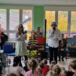 Naprzeciwko dzieci stoi para muzyków z mikrofonem i kartką w rękach