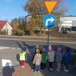 dzieci stoją w parach przy przejściu dla pieszych. w tle duży budynek