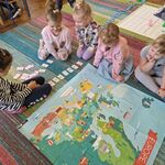 Na dywanie leży mapa Europy_ wokół niej siedzi 5 dziewczynek_ które układają z kart kod dla genibota.