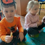 Dziewczynki siedzą na dywanie i trzymają małe świeczki.