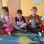 Pięcioro dzieci siedzi na dywanie_ dwie dziewczynki trzymają dymiarkę.