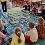Grupa dzieci siedzi na dywanie patrzą na planszę z plastrem miodu i pszczelą rodziną.