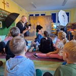 Fotograf pokazuje aparat fotograficzny dzieciom siedzącym na dywanie.