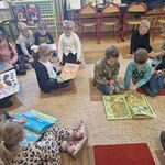 Dzieci w małych grupach siedzą na dywanie i oglądają książki.