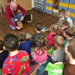 Dzieci siedzą na dywanie naprzeciwko mężczyzny_ który prezentuje budkę dla ptaków.