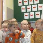 Grupa dzieci pozuje do zdjęcia_ z tyłu prace plastyczne i flaga.