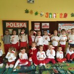 Grupa dzieci stoi z flagami na tle tablicy.
