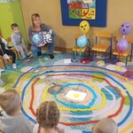na krzesełkach siedzą dzieci_ pani pokazuje przedszkolakom otwartą książkę_ obok dwaj kosmici wykonani z balonów.