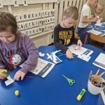 Dzieci siedzą przy stolikach_ wycinają i naklejają elementy wg kodu.