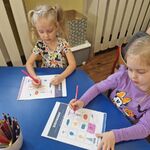 Przy stoliku siedzą dziewczynki_ kolorują pola planszy wg kodu.