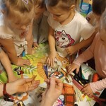 grupa dzieci pochylona nad stolikiem z guzikami_ wstążkami_ centymetrm itp.