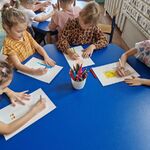 Dzieci siedzą przy stolikach i rysują swoje roboty.
