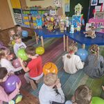Dzieci siedzą z balonami w rękach naprzeciwko robotów.