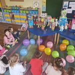 Dzieci siedzą na dywanie_ przed nimi leżą balony_ a na stole są roboty.