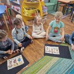 Kilkoro dzieci siedzi przy małych dywanikach z ułożonymi obrazkami.