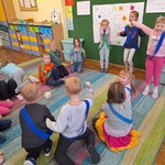 Dzieci w niebieskich szarfach pokazują gesty radości z wygranej.