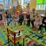 Dzieci siedzą na krzesełkach i oglądają prodiż.