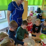 Dzieci obserwują jak dwaj chłopcy przesiewają mąkę do miski.
