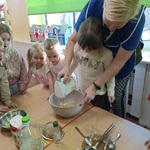Dziewczynka z pomocą opiekunki miksuje ciasto.