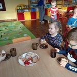 Dzieci siedzą przy stoliku i jedzą ciasto.