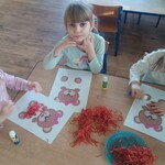 dziewczynki siedzą przy stoliku przy kartkach zna których jest obrazek misia_ pocięta bibuła.