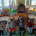 dzieci siedzą na krzesełkach_ trzymają misie w rękach podniesionych do góry.